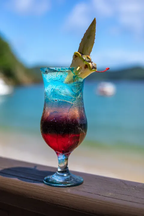 A layered blue and red cocktail on the deck rail above the beach