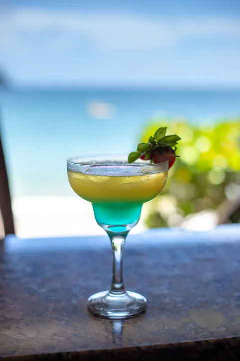 A blue and yellow cocktail with the beach behind