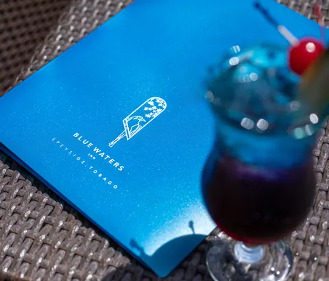 A blue cocktail with a cherry beside a Blue Waters Inn menu