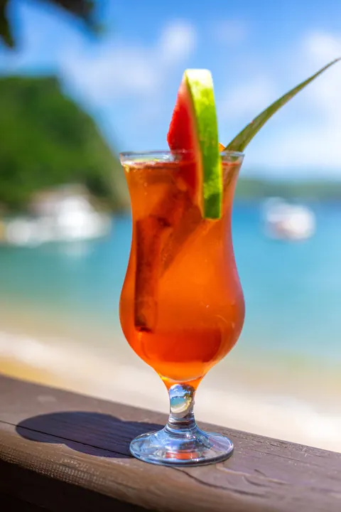 An orange cocktail with lime, with the beach behind